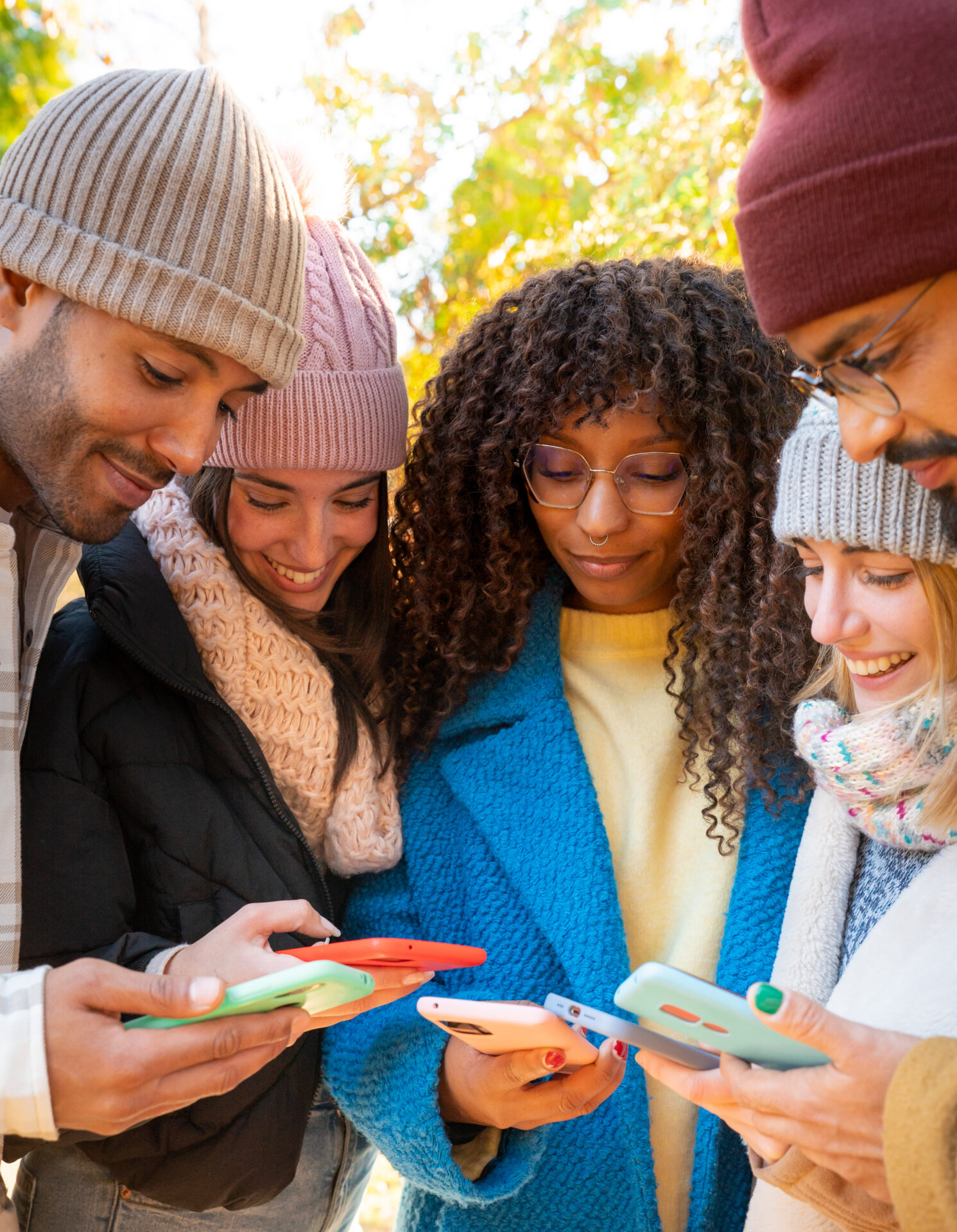 cheerful group of young friends using cell phones outdoors.